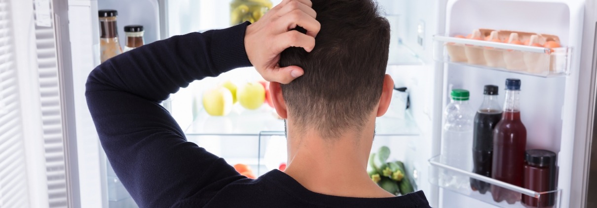 Rear View Of A Confused Young Man Looking Inside Refrigerator