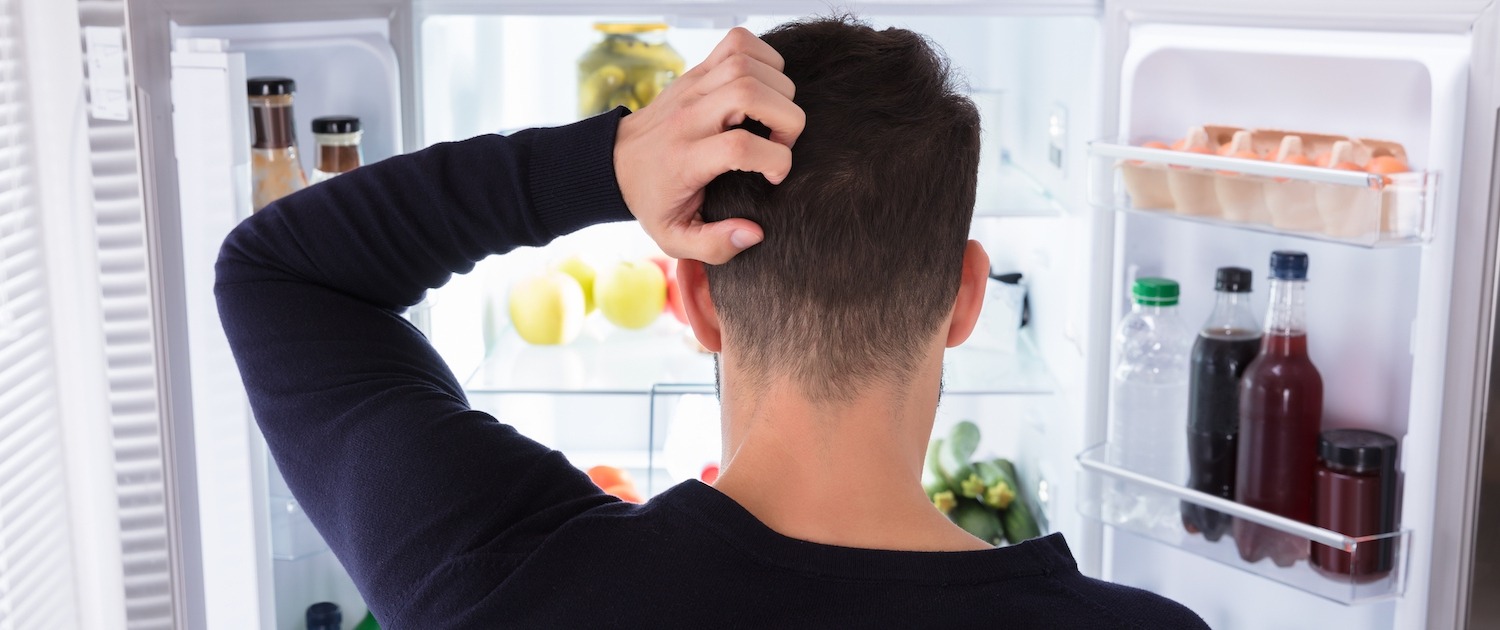 Rear View Of A Confused Young Man Looking Inside Refrigerator