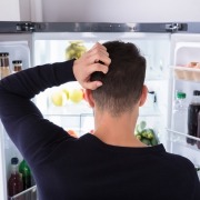 Rear View Of A Confused Young Man Looking Inside Refrigerator