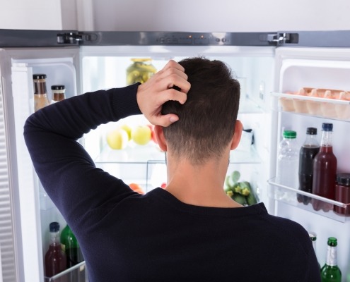 Rear View Of A Confused Young Man Looking Inside Refrigerator