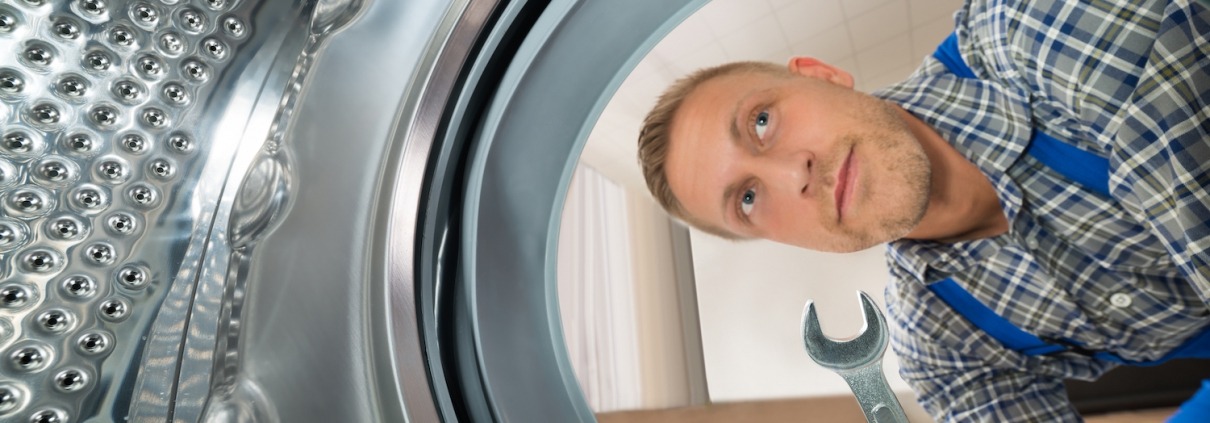 Young Repairman With WrenchLooking Inside The Washing Machine