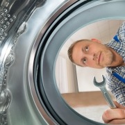 Young Repairman With WrenchLooking Inside The Washing Machine