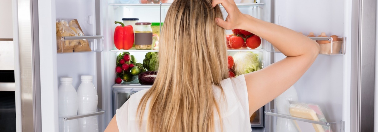blond woman scratching head in front of refrigerator too cold