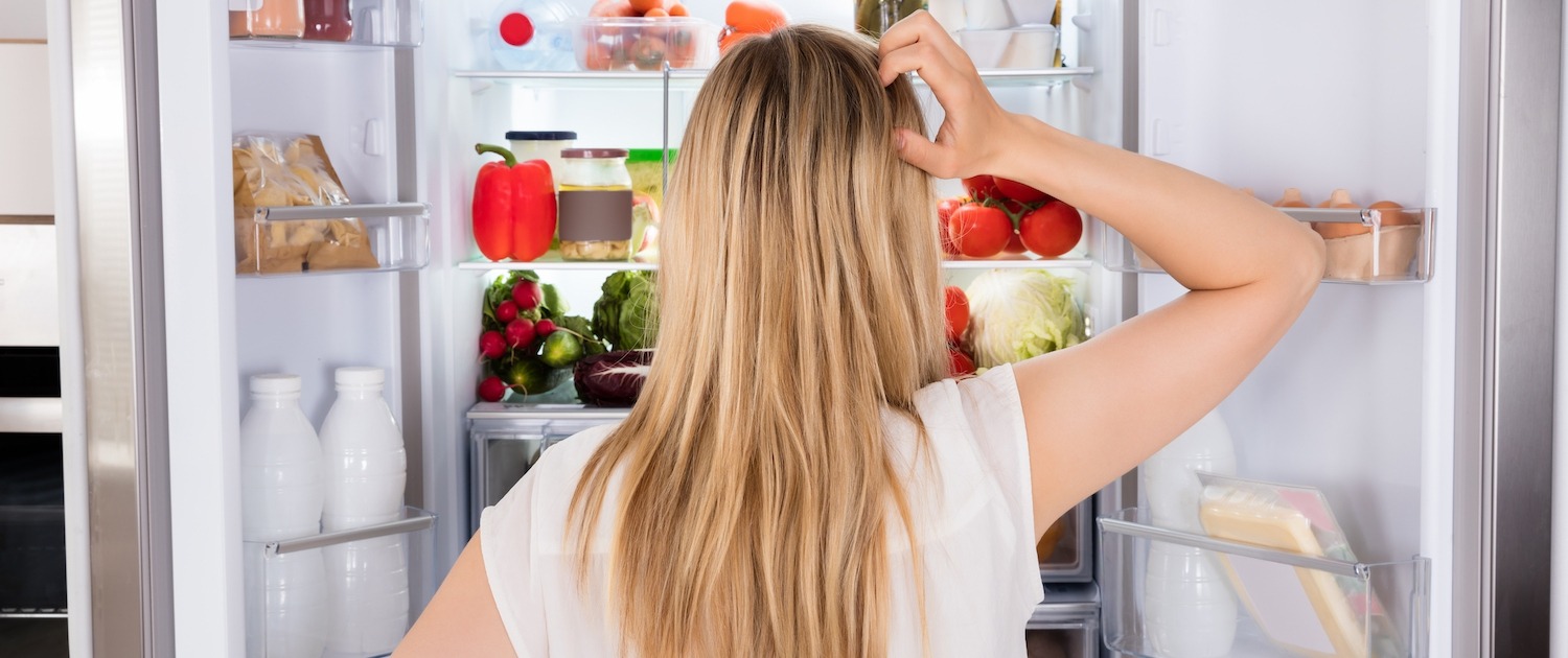 blond woman scratching head in front of refrigerator too cold