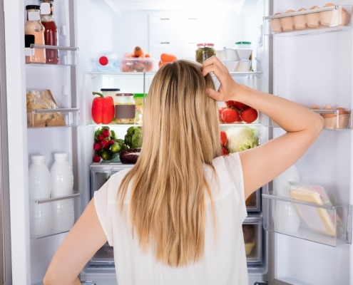 blond woman scratching head in front of refrigerator too cold