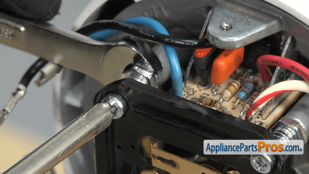 Gloved hands using a Phillips screwdriver and a wrench inside a KitchenAid mixer
