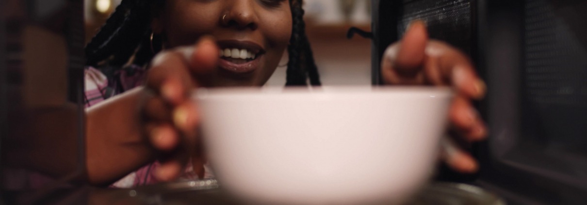 African American woman placing a ceramic bowl into the microwave.