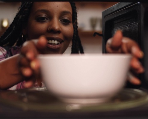 African American woman placing a ceramic bowl into the microwave.