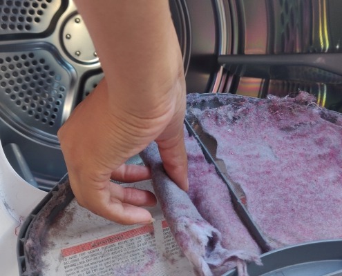 Hand removing lint from the lint filter of a dryer