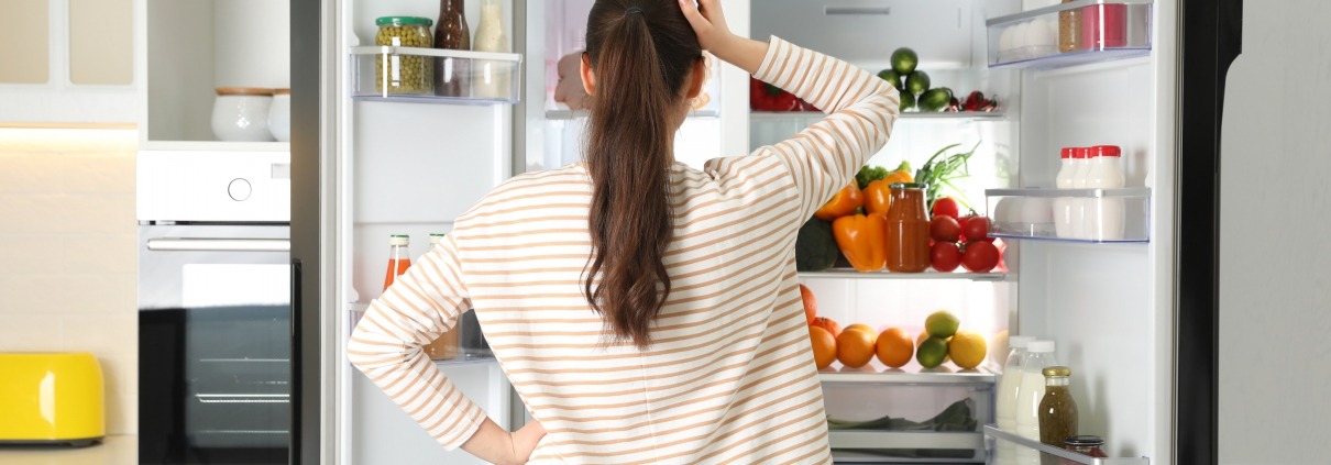 Woman standing in front of open refrigerator scratching head