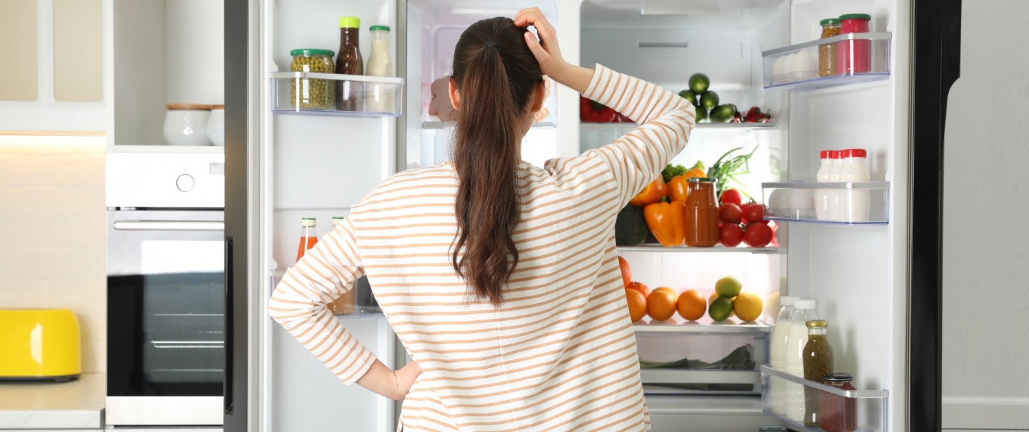 Woman standing in front of open refrigerator scratching head