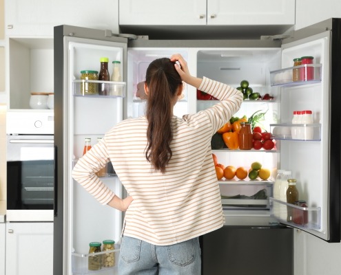 Woman standing in front of open refrigerator scratching head