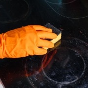 Orange glove with a sponge on a dirty ceramic glass cooktop