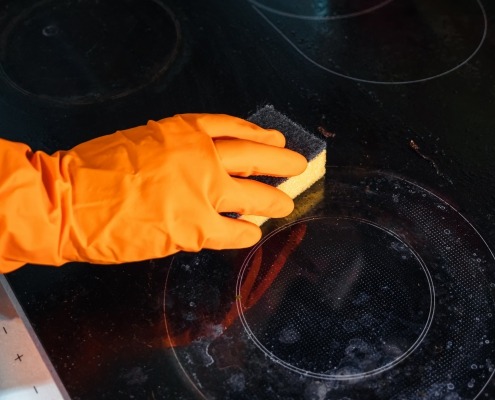 Orange glove with a sponge on a dirty ceramic glass cooktop