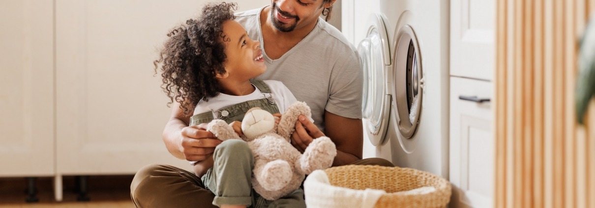 Father and some folding laundry sitting in the floor in front of the washer