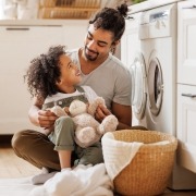 Father and some folding laundry sitting in the floor in front of the washer