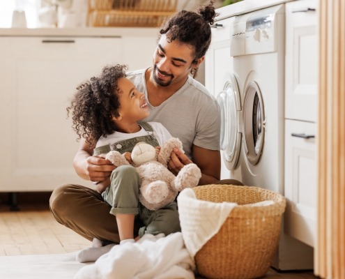 Father and some folding laundry sitting in the floor in front of the washer