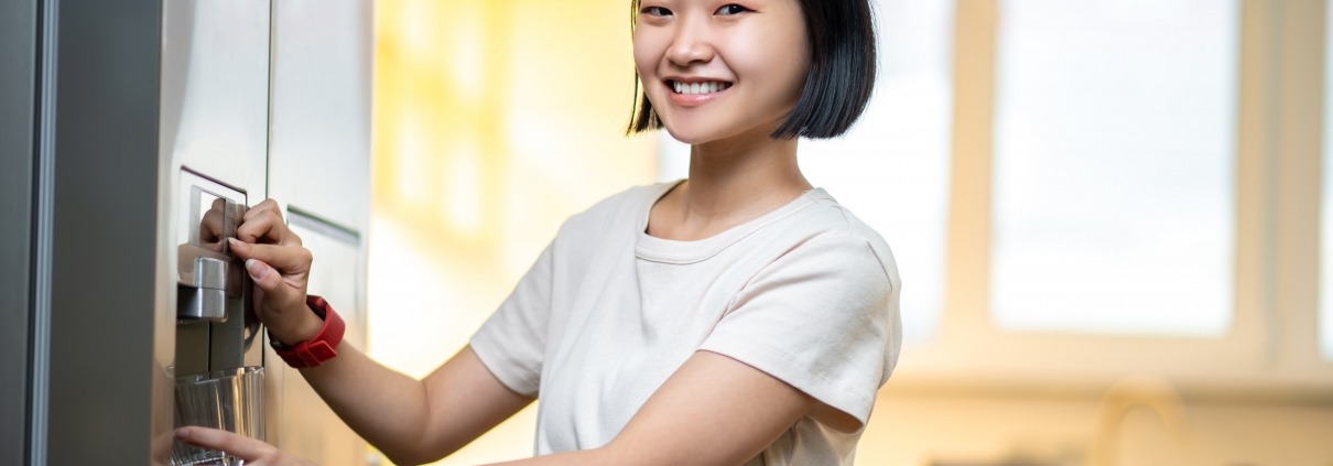 smiling person filling a glass with filtered water from the fridge water dispenser