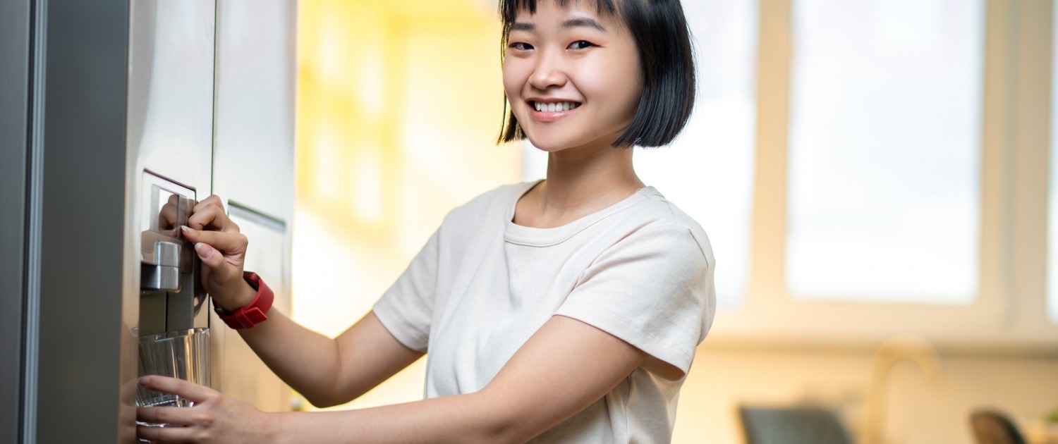 smiling person filling a glass with filtered water from the fridge water dispenser