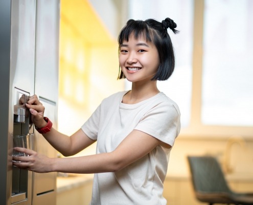 smiling person filling a glass with filtered water from the fridge water dispenser