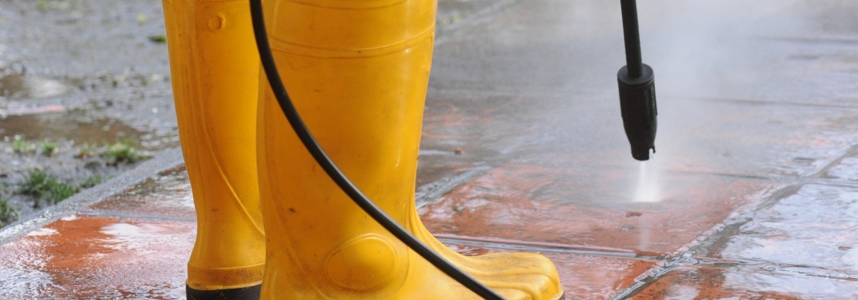 person wearing yellow rubber boots with high-pressure water nozzle cleaning the dirt in the tiles. Image by wirestock on freepik.com