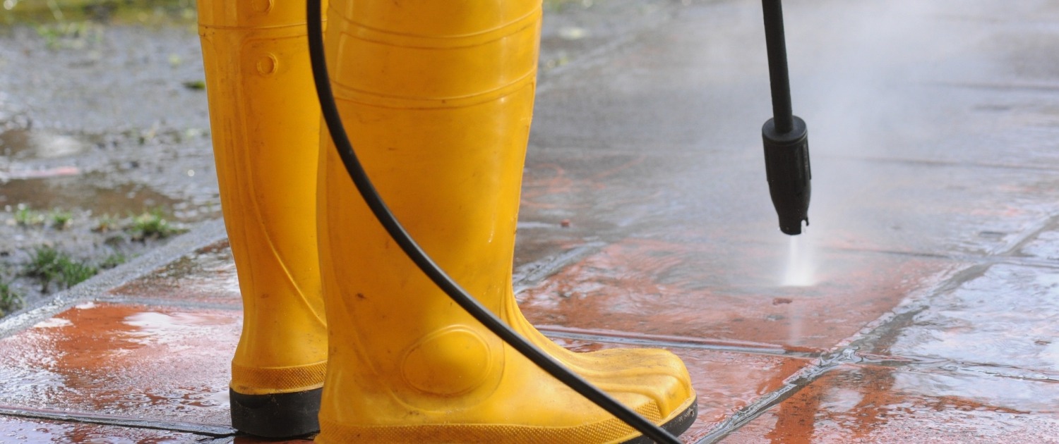 person wearing yellow rubber boots with high-pressure water nozzle cleaning the dirt in the tiles. Image by wirestock on freepik.com