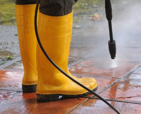 person wearing yellow rubber boots with high-pressure water nozzle cleaning the dirt in the tiles. Image by wirestock on freepik.com
