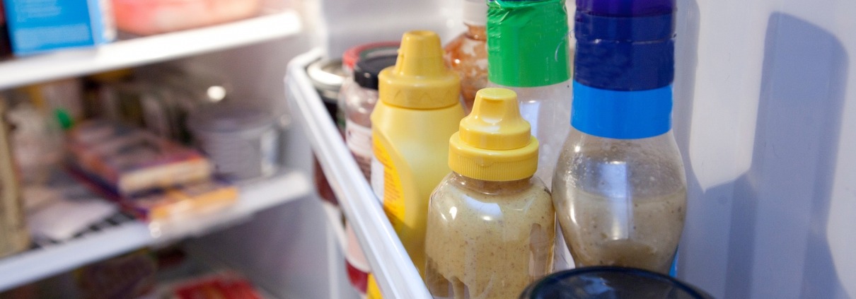condiment bottles on a refrigerator shelf behind the fridge door shelf bar