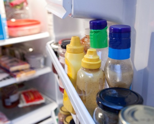 condiment bottles on a refrigerator shelf behind the fridge door shelf bar
