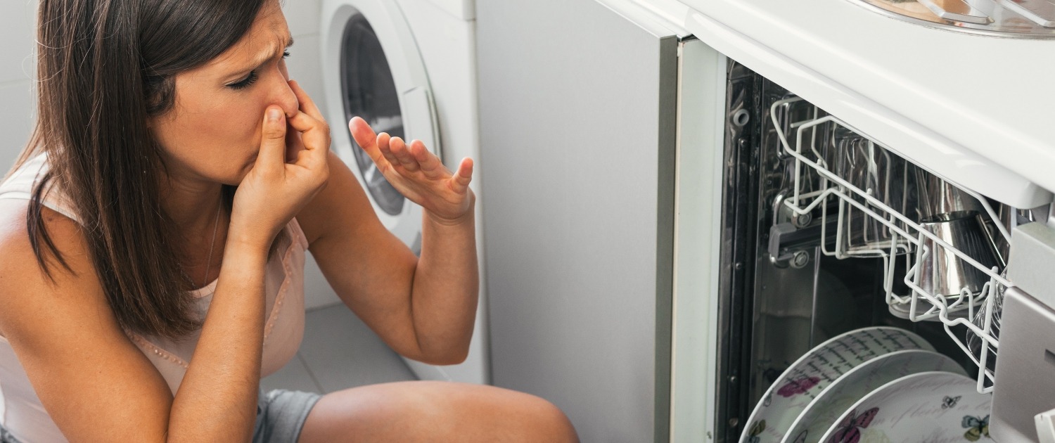 Woman making gestures of bad smell when opening her dishwasher