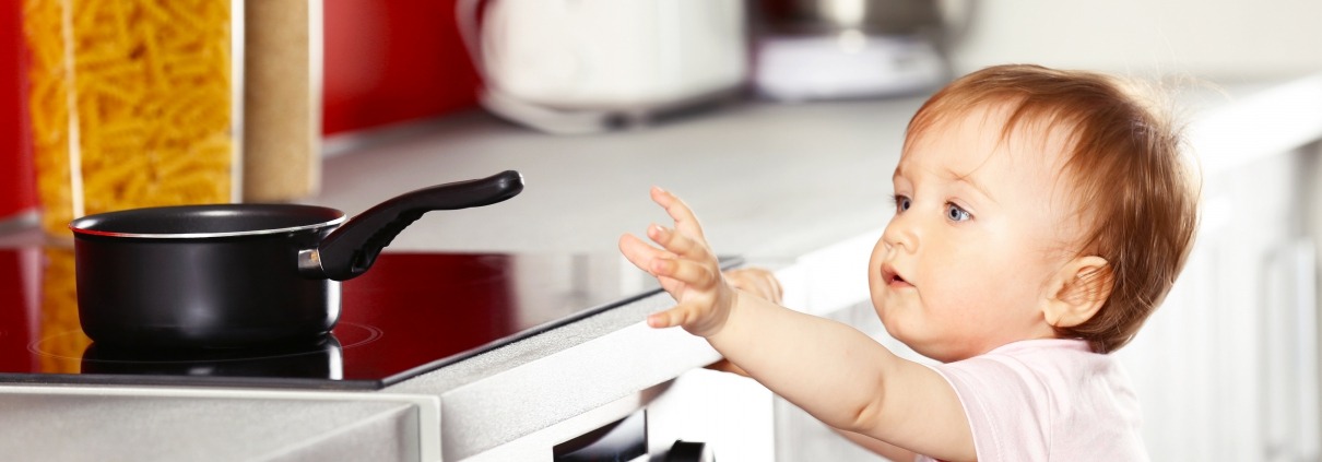 child reaching for a pot handle on the stove in the kitchen