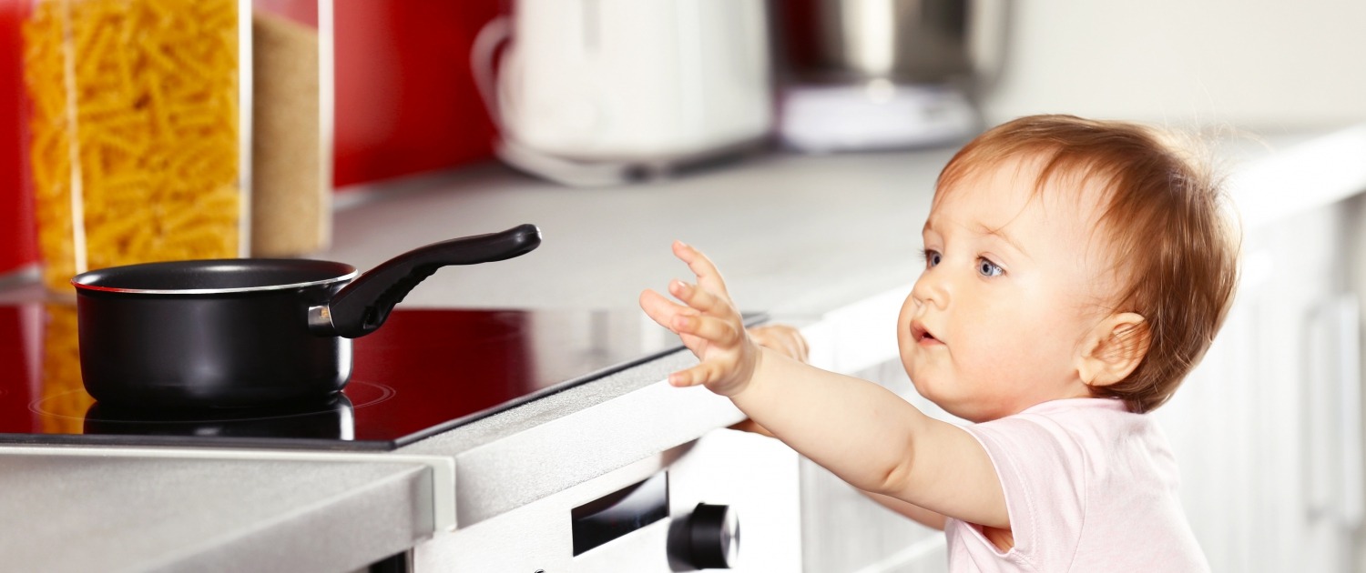 child reaching for a pot handle on the stove in the kitchen