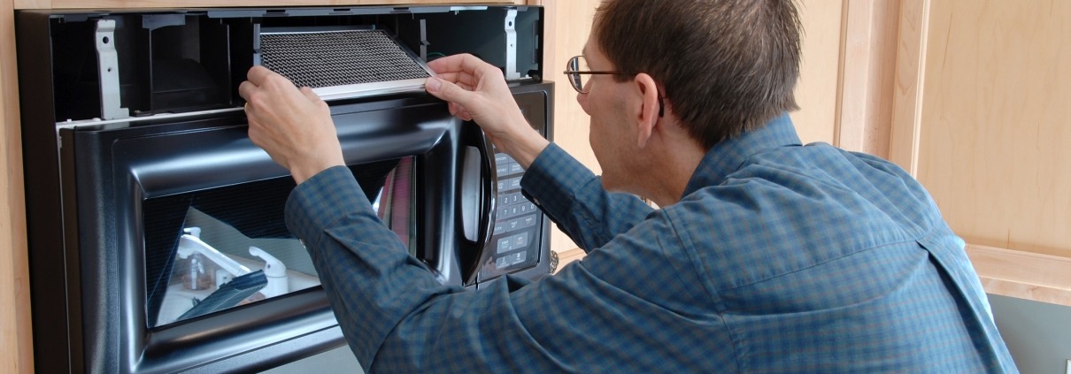 Man Demonstrating How To Remove And Clean A Microwave Grease Filter