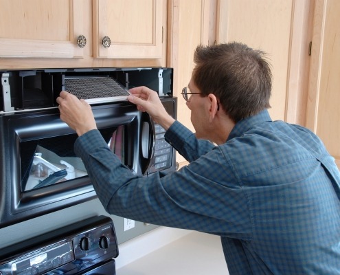 Man Demonstrating How To Remove And Clean A Microwave Grease Filter