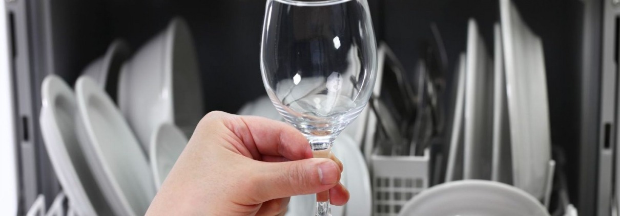 person holding glass in front of loaded dishwasher