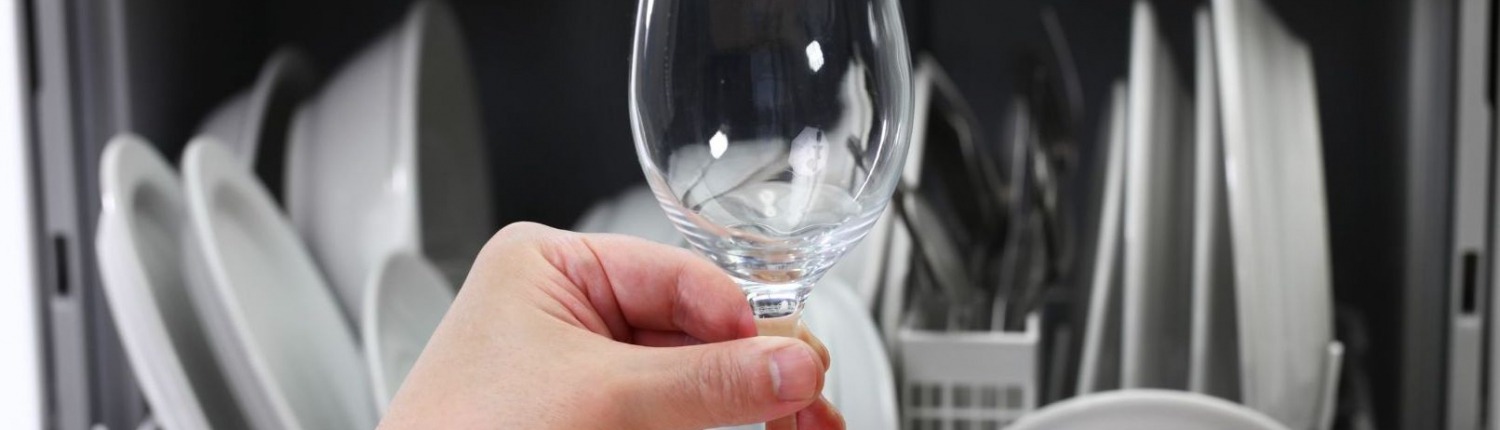 person holding glass in front of loaded dishwasher