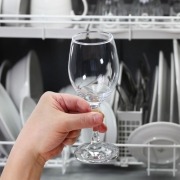 person holding glass in front of loaded dishwasher