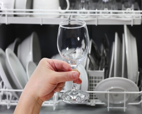 person holding glass in front of loaded dishwasher