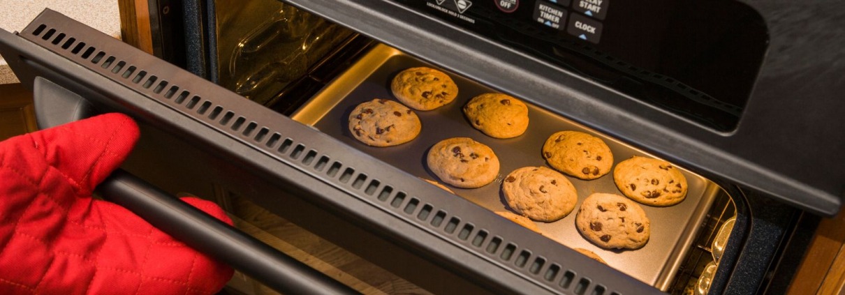open oven with cookies inside on pan and person holding door with oven mitt