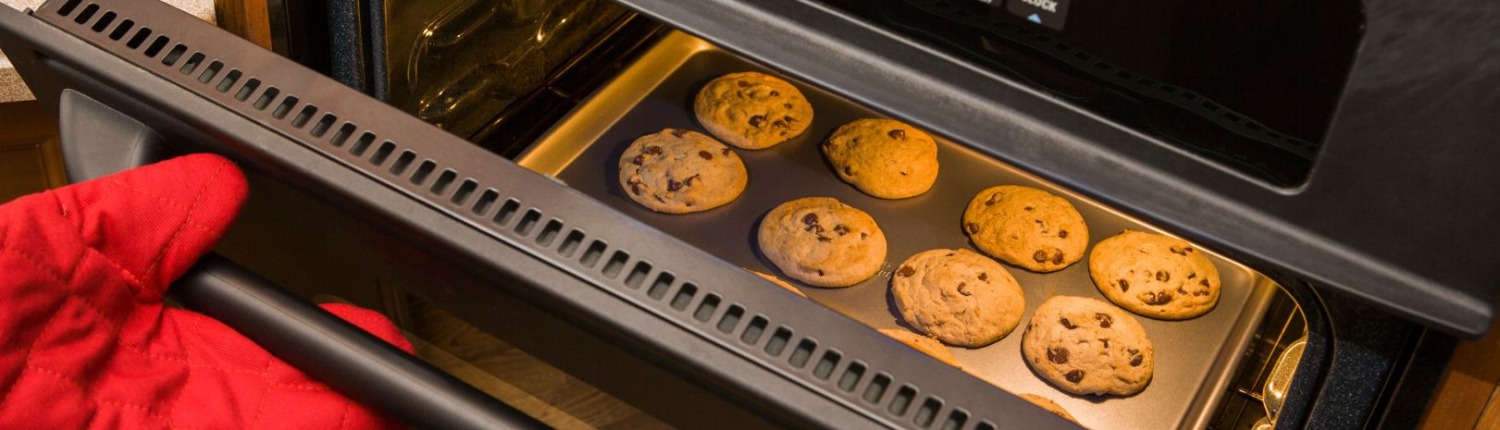 open oven with cookies inside on pan and person holding door with oven mitt