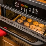 open oven with cookies inside on pan and person holding door with oven mitt