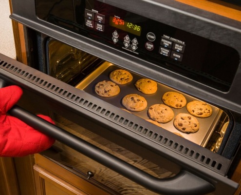 open oven with cookies inside on pan and person holding door with oven mitt