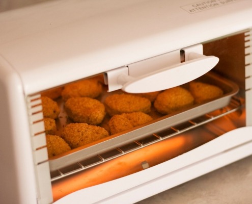 closed toaster oven with breaded meat cooking inside