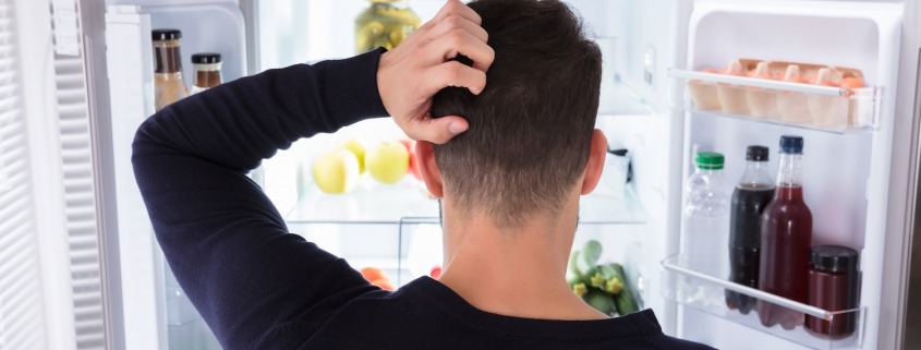 Rear View Of A Confused Young Man Looking Inside Refrigerator