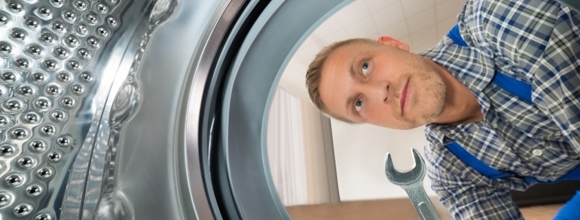 Young Repairman With WrenchLooking Inside The Washing Machine