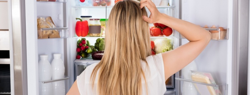 blond woman scratching head in front of refrigerator too cold