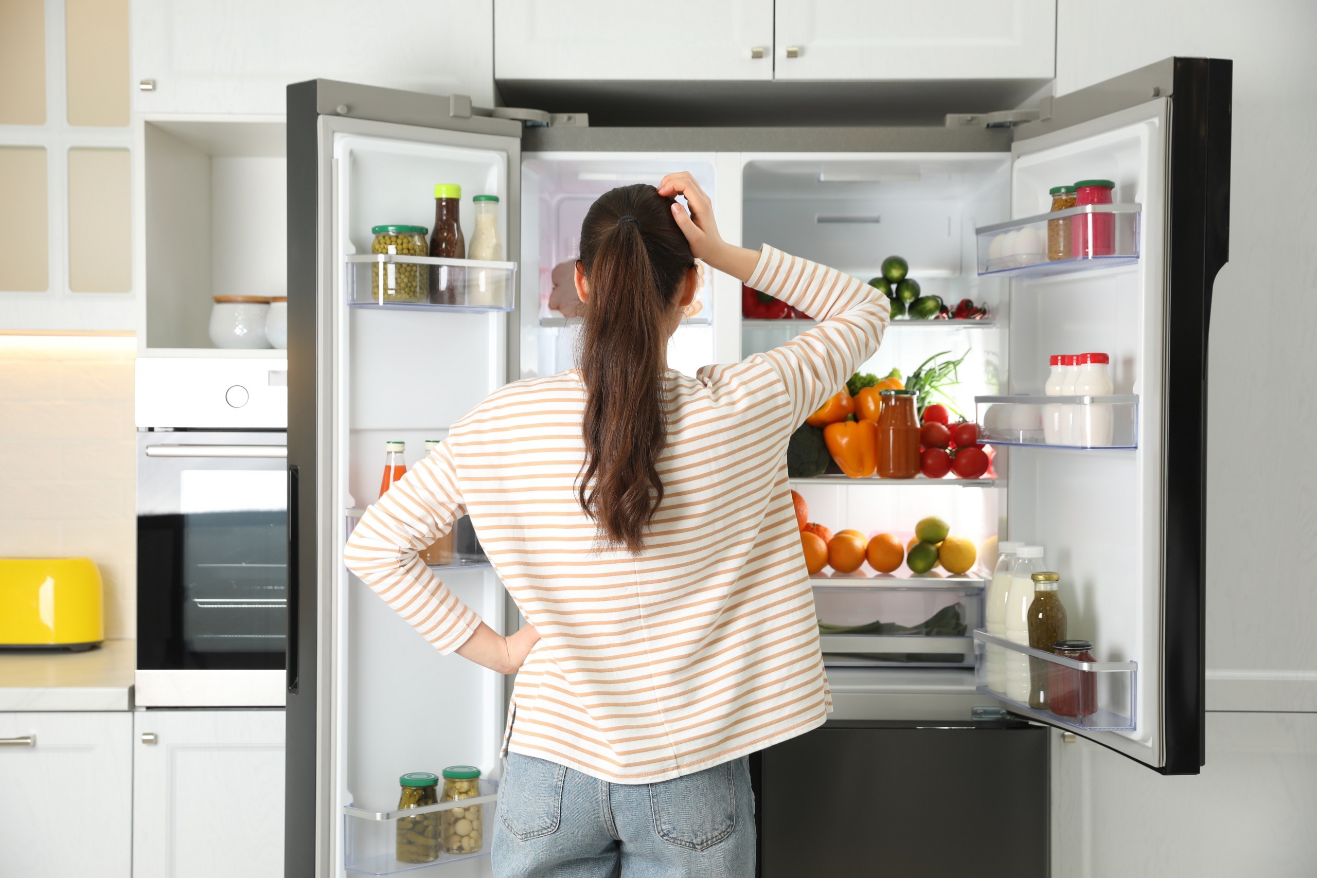 Woman standing in front of open refrigerator scratching head
