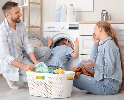 A mother, father, and child do laungry together in front of high efficiency washing machine
