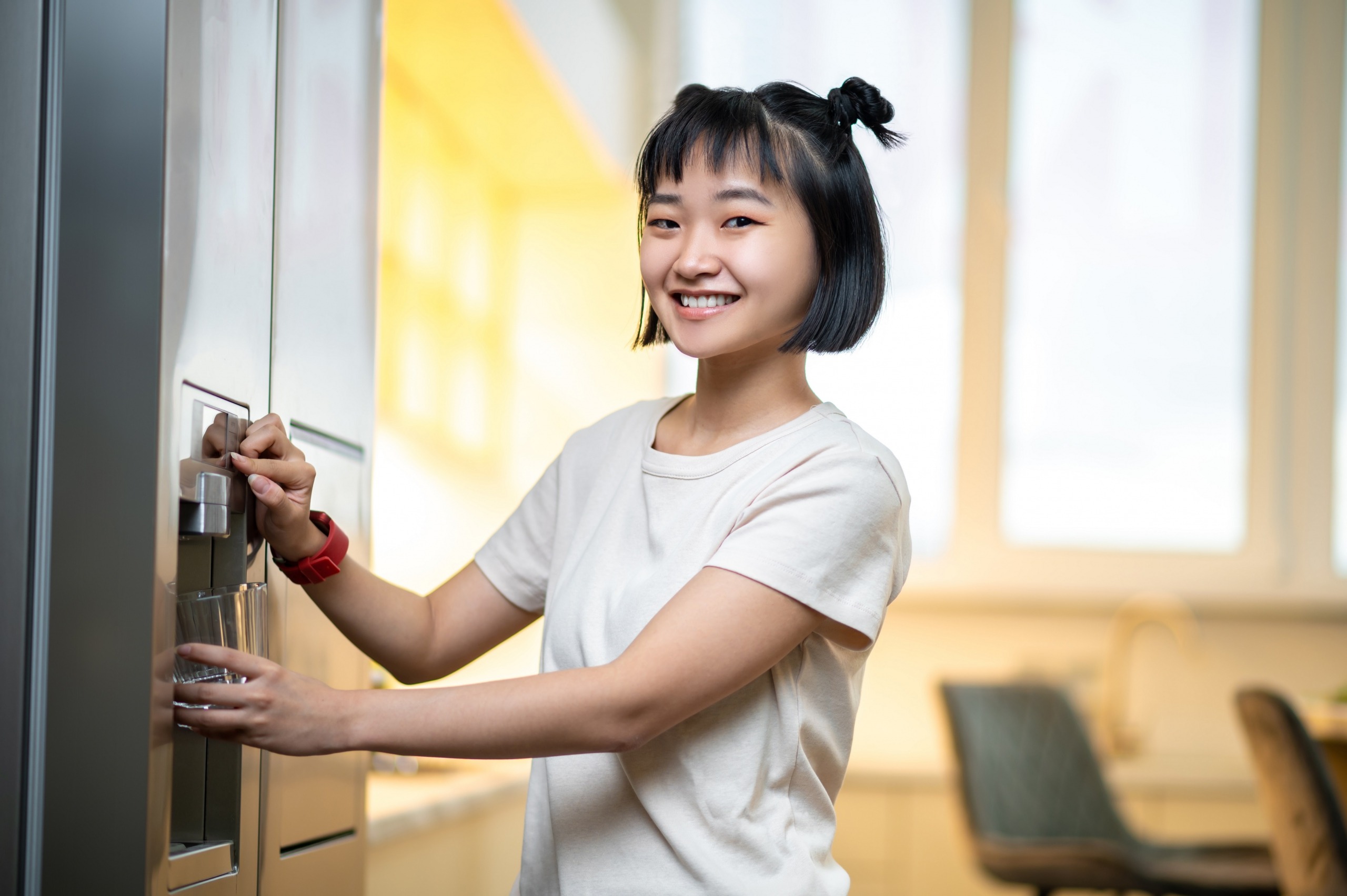 smiling person filling a glass with filtered water from the fridge water dispenser