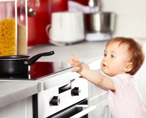 child reaching for a pot handle on the stove in the kitchen